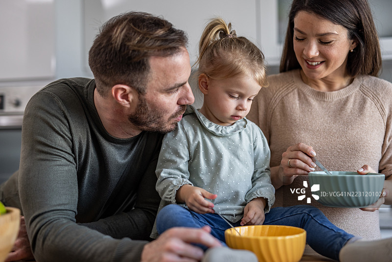 一家人在厨房一起吃早餐：慈爱的父母看着女儿享受美食图片素材