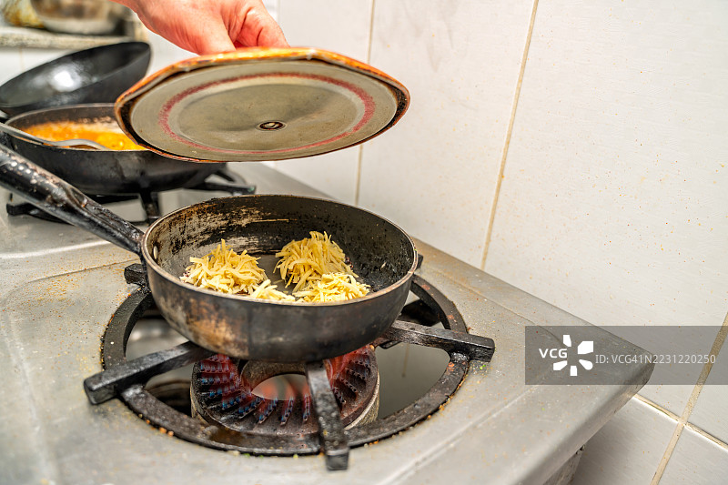 厨师在秘鲁餐厅厨房中揭开煎锅盖，锅里放着土豆煎饼。图片素材