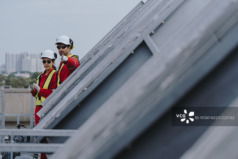 工业工程师团队在施工现场维护管道、阀门、空调、制冷和暖通空调系统。穿着红色安全制服的男性技术人员正在检查管道阀门。图片素材