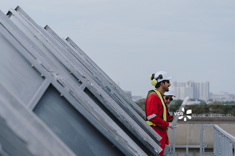 工业工程师团队在施工现场维护管道、阀门、空调、制冷和暖通空调系统。穿着红色安全制服的男性技术人员正在检查管道阀门。图片素材