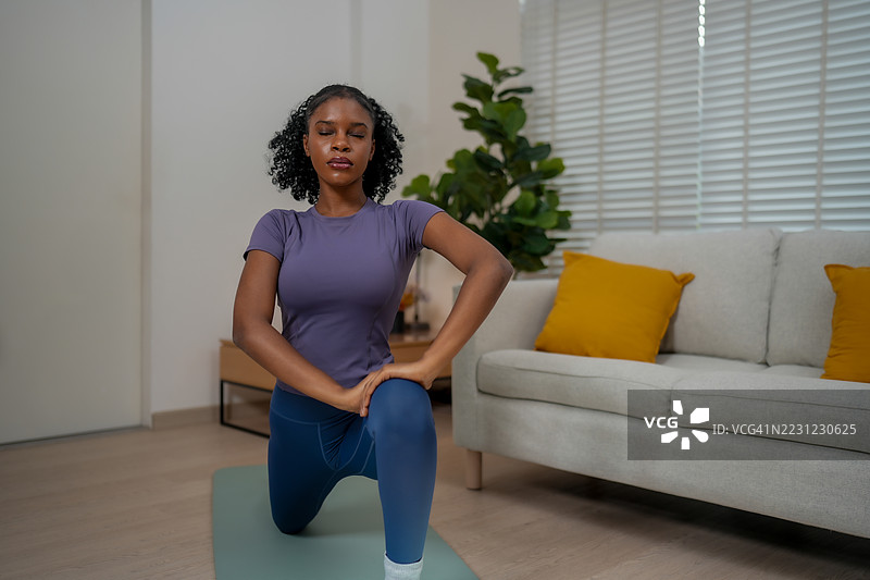 黑人女性在室内锻炼，专注而坚定地练习瑜伽。宁静的环境提升了她的体验，她在伸展和寻找平衡。图片素材