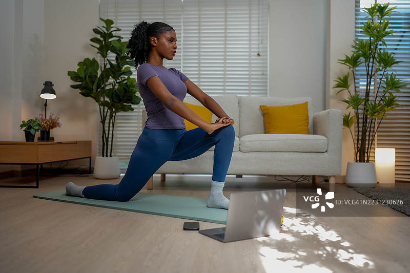 黑人女性在室内锻炼，专注而坚定地练习瑜伽。宁静的环境提升了她的体验，她在垫子上优雅地伸展。图片素材