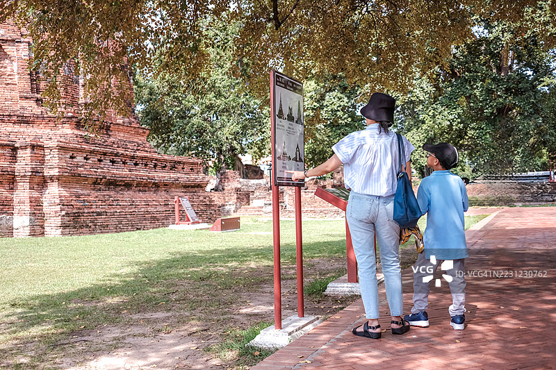年轻的孩子和他的母亲站在一起，望着大城省的玛哈泰寺的信息牌图片素材