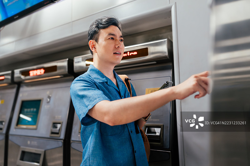 年轻的亚洲男子在火车站自助售票机上使用手机支付购票。非接触式支付与交通。电子火车票。信用卡支付。NFC技术，轻触即付的概念。图片素材