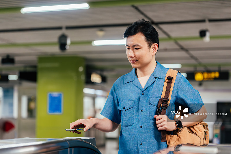 自信的年轻亚洲商人在票闸处用智能手机快速便捷地进行无接触支付，购买地铁票。电子火车票。信用卡支付。NFC技术，轻触即付的概念。图片素材