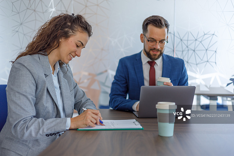 女商人正在签署合同，她的合作伙伴在一旁观看。图片素材