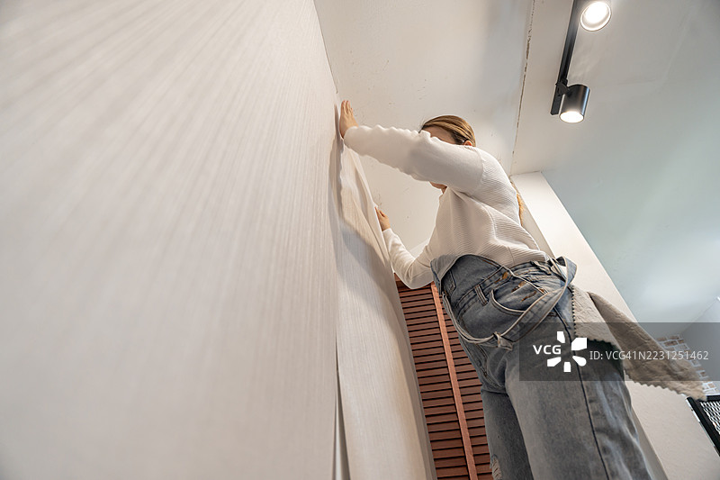 亚洲女性在客厅贴壁纸。DIY和家居装饰。图片素材