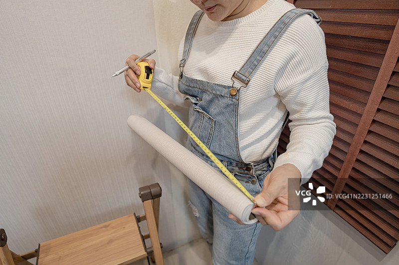 亚洲女性在客厅贴壁纸。DIY和家居装饰。图片素材