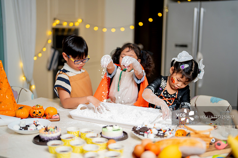 亚洲家庭在家制作饼干和蛋糕庆祝万圣节。孩子在烹饪课上向妈妈学习。图片素材
