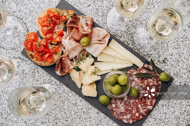 肉类、奶酪和橄榄的拼盘展示在石板托盘上，搭配酒杯，营造出一种精致的用餐体验。图片素材