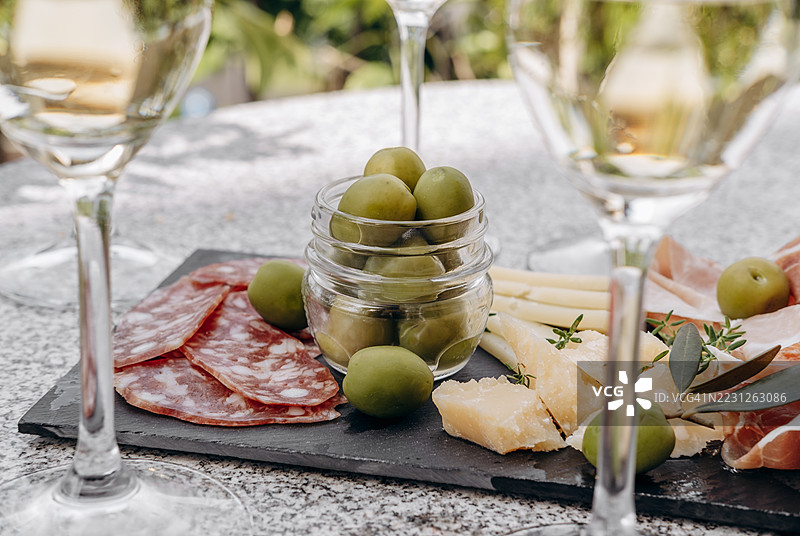 肉类、奶酪和橄榄的拼盘展示在石板托盘上，搭配酒杯，营造出一种精致的用餐体验。图片素材