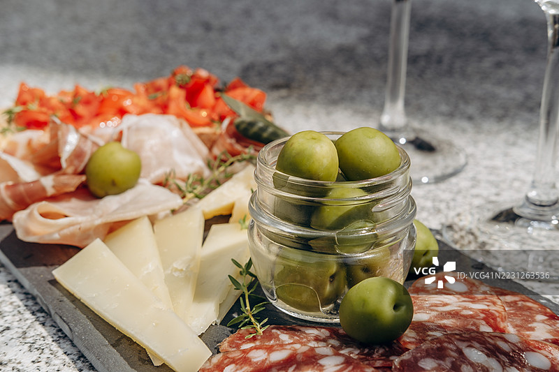 肉类、奶酪和橄榄的拼盘展示在石板托盘上，搭配酒杯，营造出一种精致的用餐体验。图片素材