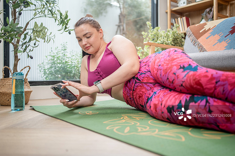 放松的胖女人在家健身后休息，她正在使用智能手机。肥胖的女人想要减肥并燃烧卡路里。图片素材