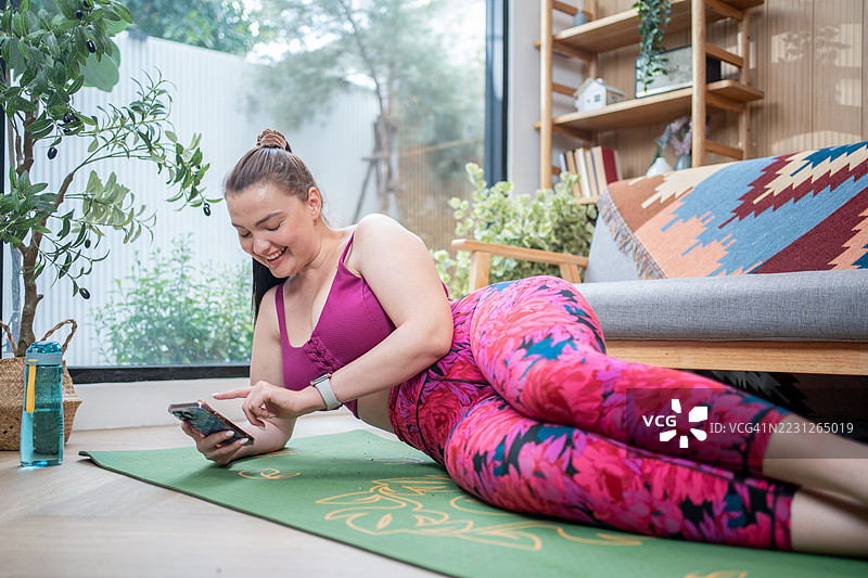 放松的胖女人，在家健身训练后使用智能手机休息。肥胖的女人想减肥和燃烧卡路里。图片素材