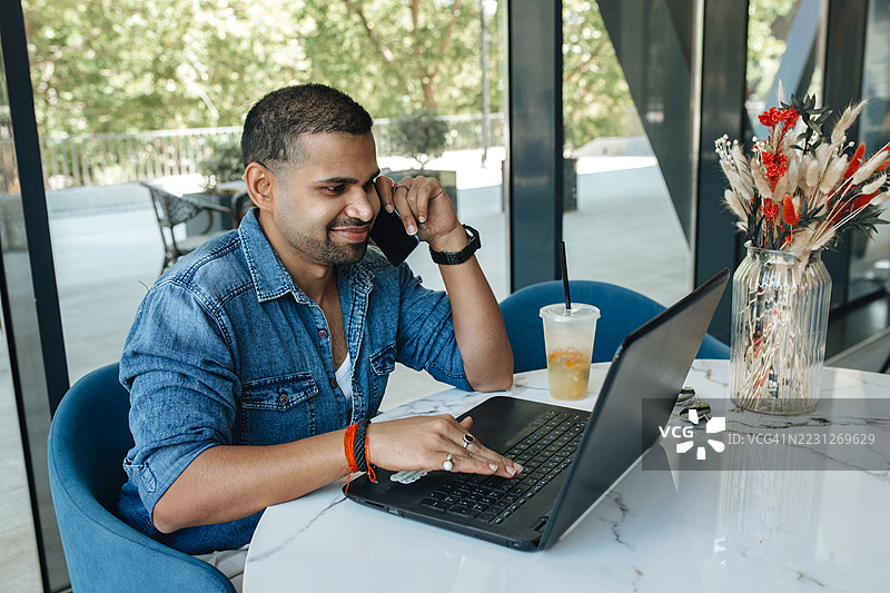 年轻印度男子在咖啡馆使用笔记本电脑的特写肖像。图片素材