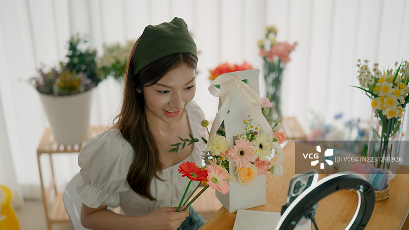 年轻的亚洲女性在花店里一边卖花和花束，一边进行直播。图片素材