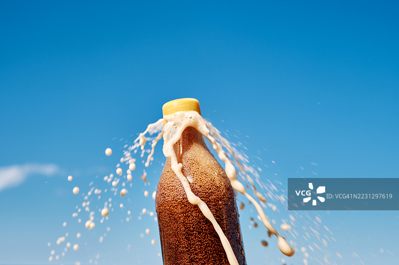 一瓶装有棕色碳酸饮料的塑料瓶从瓶盖下喷出，冲向天空。图片素材