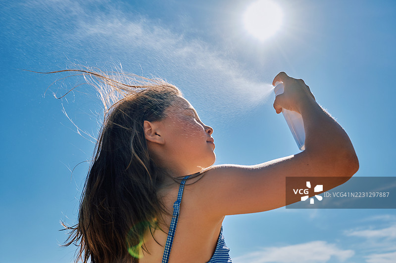 女孩在炎热中用喷雾喷洒温泉水来清爽自己。图片素材