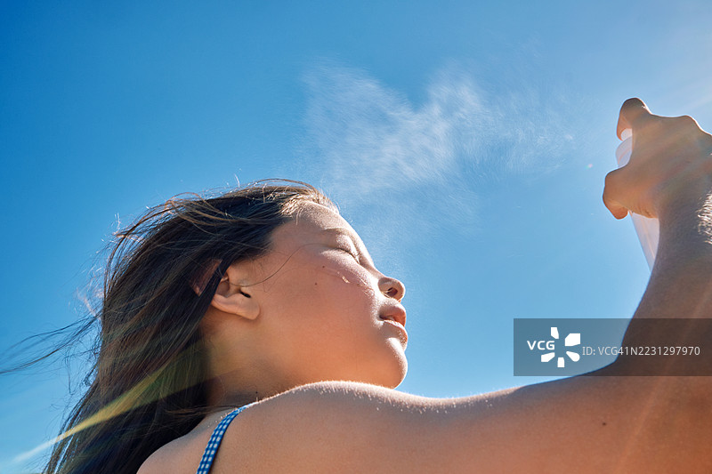 女孩在炎热中用喷雾喷洒温泉水来清新自己。图片素材