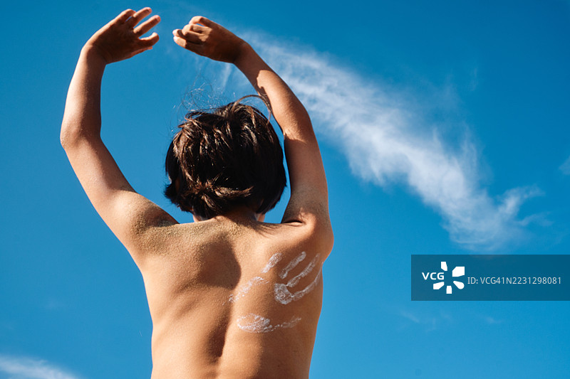 一个青少年男孩的背上印着手印形状的防晒霜，背景是天空。图片素材