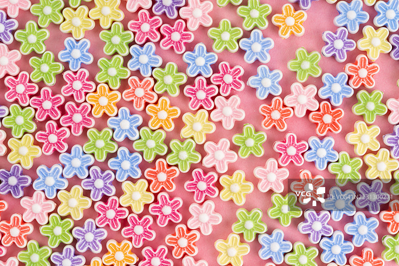 粉色背景上的各种彩色花形珠子。图片素材