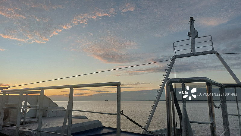 从渡轮甲板栏杆和船体结构上俯瞰的日落海景，天空呈粉彩色，海洋地平线宁静。图片素材