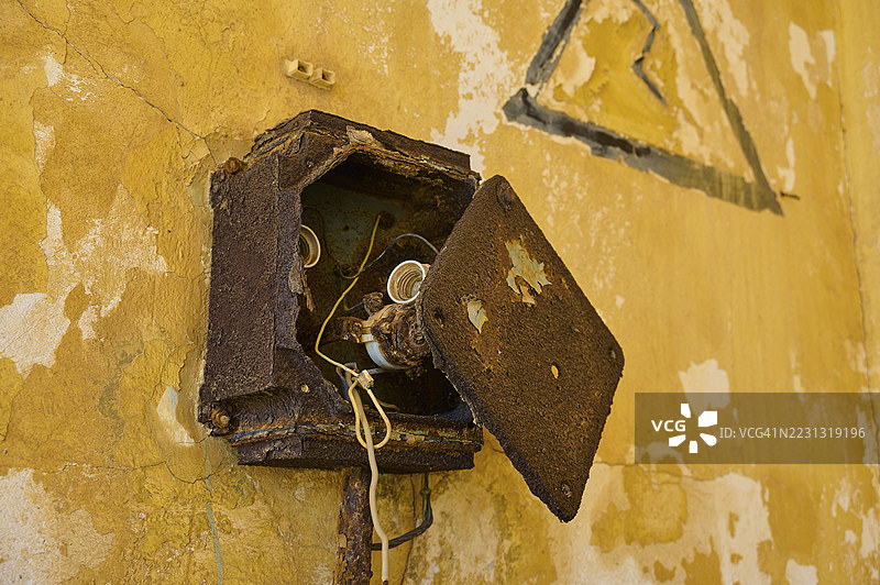 翻开的、生锈的开关盒，位于饱经风霜的墙壁上，废弃之地，意大利旧军事营地，二战，第二次世界大战，阿基奥斯·乔治奥斯，阿斯蒂帕莱亚，阿斯蒂帕莱亚，阿斯蒂帕莱亚，佐泽卡尼斯，希腊群岛，希腊图片素材