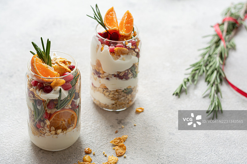 玻璃罐中的酸奶配格兰诺拉麦片、新鲜水果、橘子和蔓越莓。圣诞气氛，节日。健康早餐，零食。外带概念。图片素材