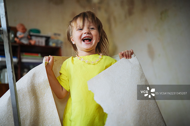 快乐的孩子：穿着黄色T恤的孩子高兴地跳跃，手里拿着墙纸碎片。图片素材