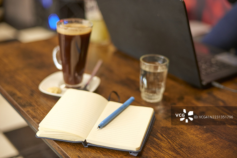 桌子上有笔记本、钢笔、咖啡和水杯，背景是笔记本电脑图片素材