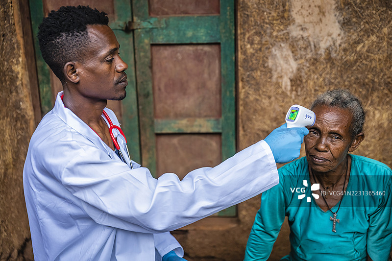 男性医生在东非偏远村庄为一位老年女性测量体温图片素材