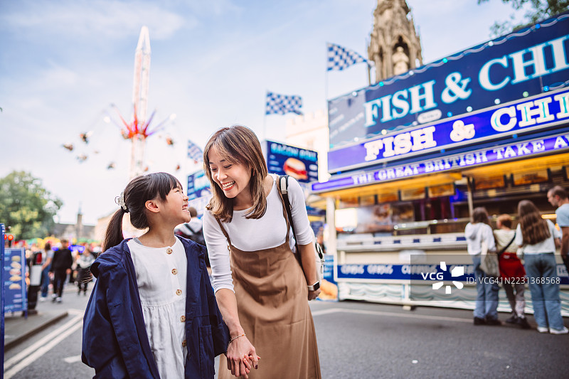 快乐的母女在街头集市上鱼和薯条摊位前一起欢笑图片素材