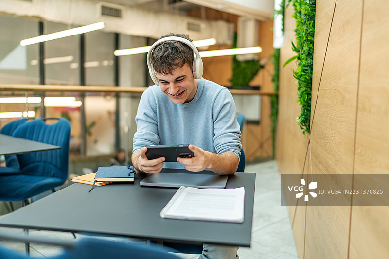 年轻男子在共享办公空间里戴着耳机玩手机游戏图片素材
