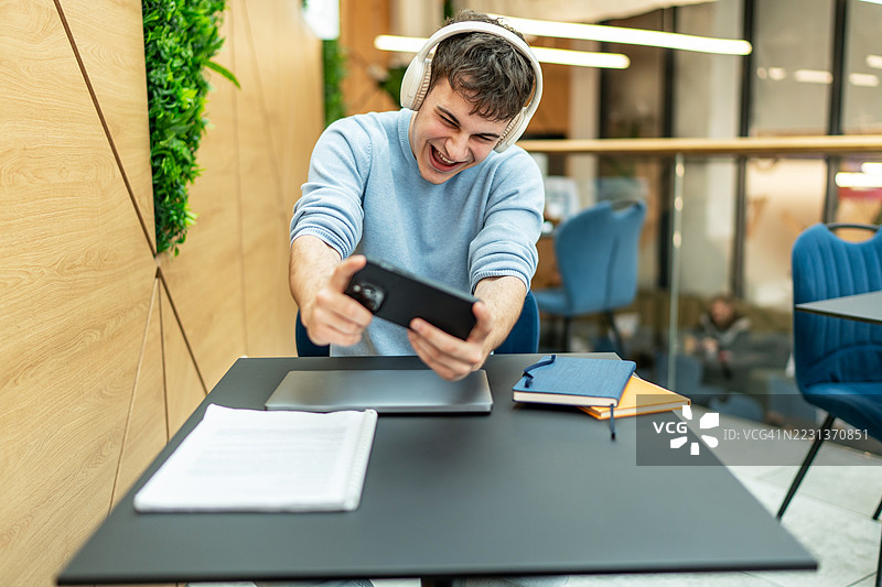 兴奋的学生在大学餐厅玩手机游戏图片素材