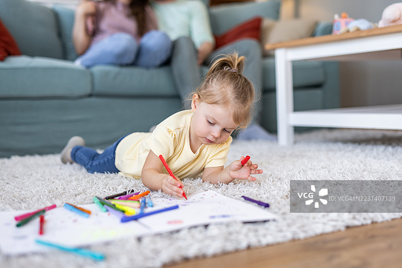 可爱的小女孩在家里躺在地板上用马克笔画画图片素材