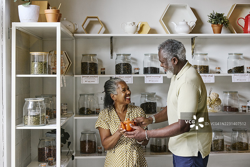 微笑的成熟男性将茶壶递给女性朋友图片素材