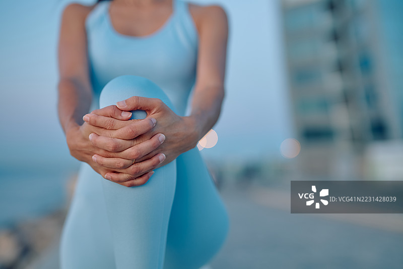 年轻女运动员在户外训练时受伤，捂着膝盖。图片素材