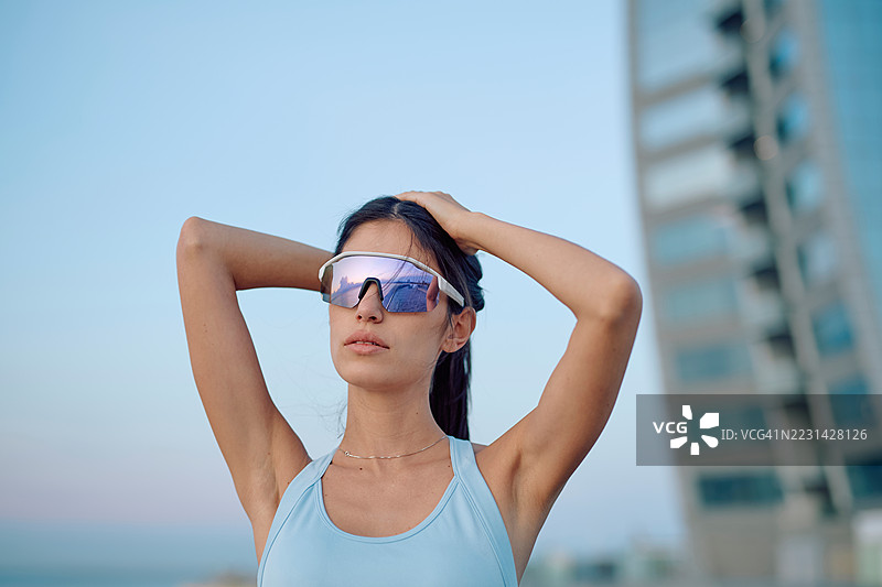 运动女性在城市中调整头发并佩戴太阳镜图片素材