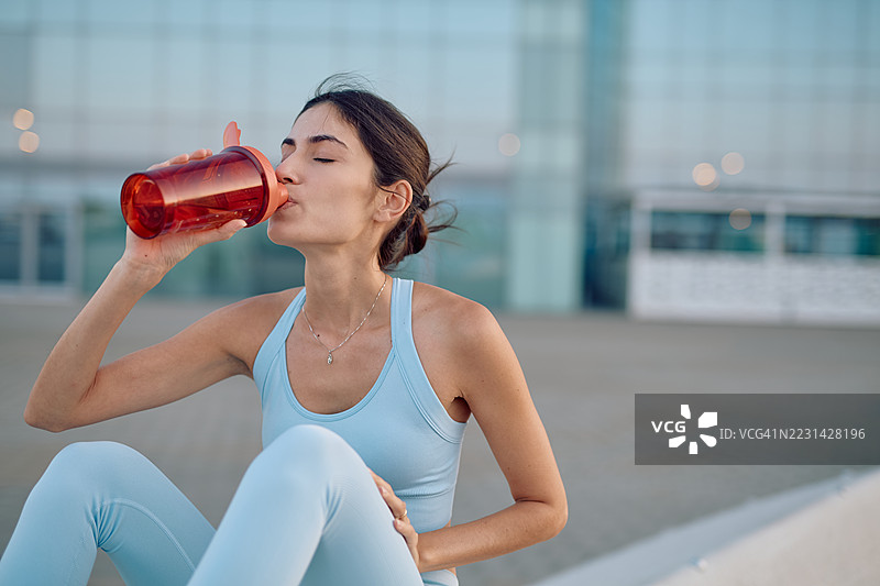 年轻的女运动员在户外训练后喝水图片素材