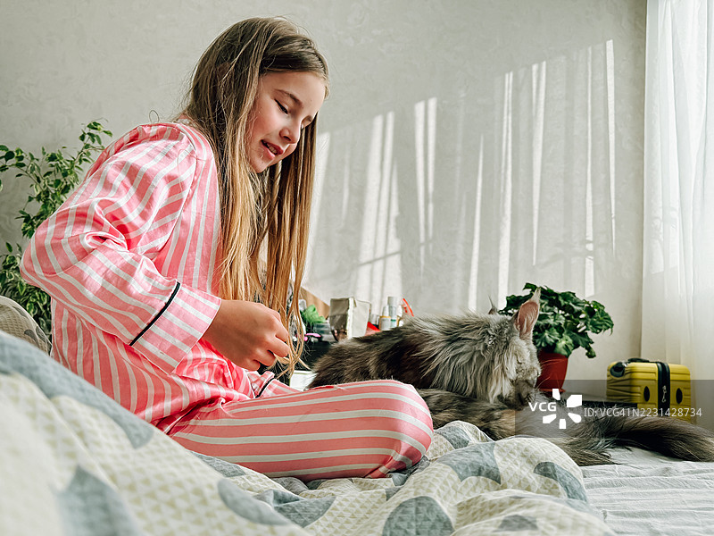 微笑的女孩在卧室里与她的缅因猫亲密互动图片素材
