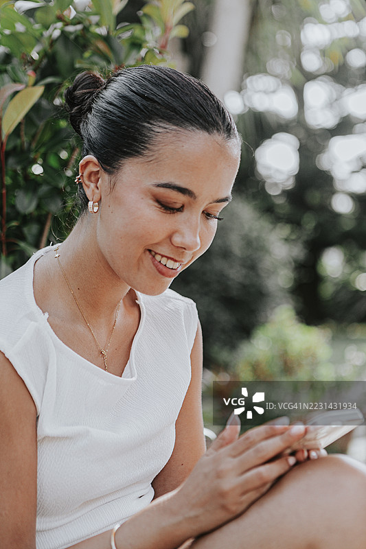 年轻漂亮的女性在户外轻松地用智能手机发信息图片素材