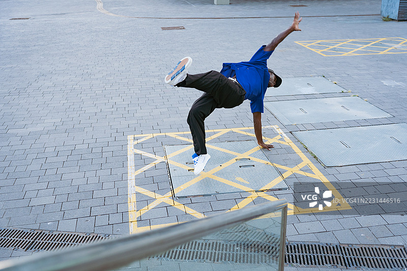年轻男子在充满活力的城市街道上倒立表演令人印象深刻的霹雳舞动作，展现出技巧、活力和创造力图片素材