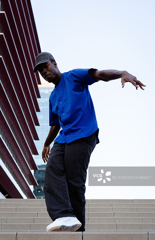 年轻舞者在城市环境中的台阶上表演街舞，背景是一座现代建筑。图片素材