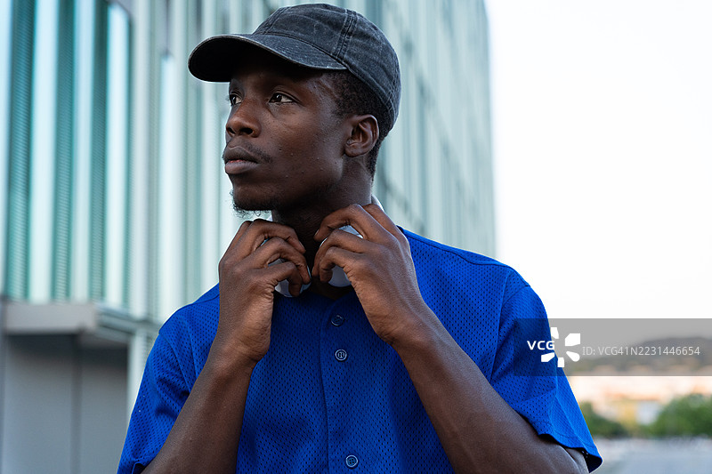 年轻的黑人男性戴着耳机和帽子，站在现代建筑旁，沉浸在音乐中，陷入沉思。图片素材