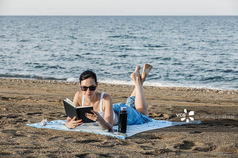一位女性在海滩上阅读一本书图片素材