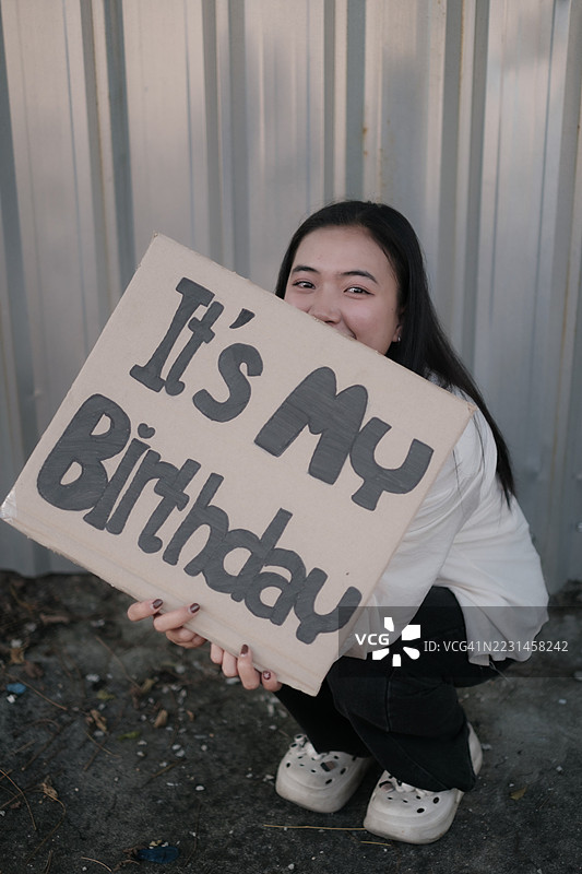 一位亚洲女性在她的生日上举着“我的生日”标志。图片素材