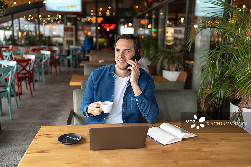 年轻的自由职业者在咖啡馆里打电话并喝咖啡图片素材
