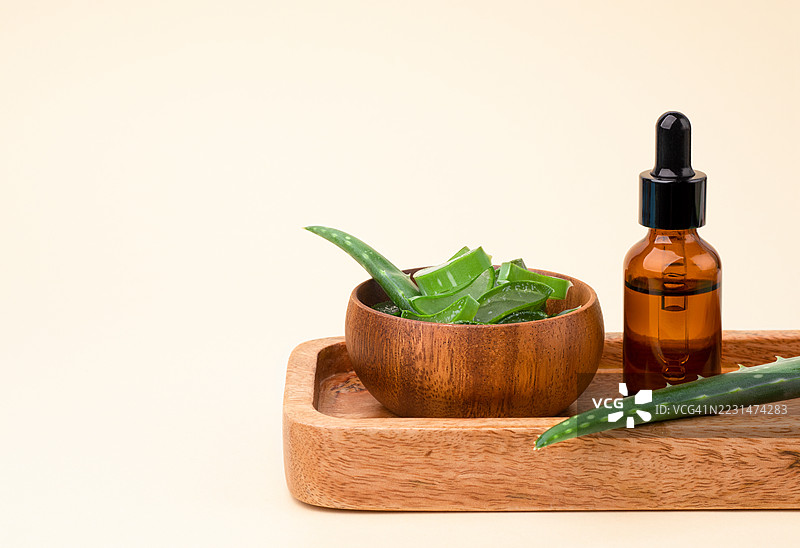 木碗中的芦荟叶，木盘上的玻璃化妆瓶。浅米色背景，留有空白空间。图片素材
