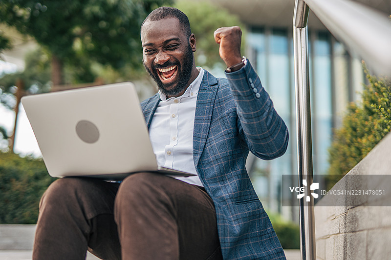 兴奋的商人在户外用笔记本电脑庆祝成功图片素材