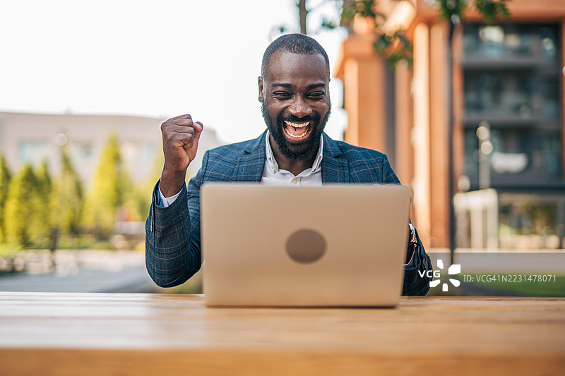 兴奋的商人在户外用笔记本电脑庆祝成功图片素材